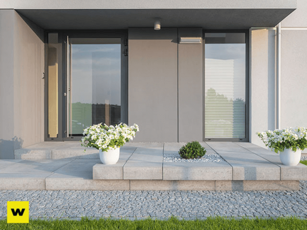 Moderner Hauseingang mit großen Glasflächen, Steinterrasse und dekorativen Blumenkübeln.